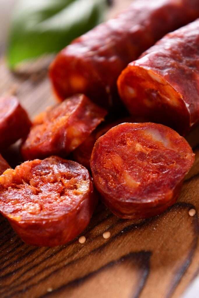 Close-up of sliced chorizo sausage on a wooden surface with small mustard seeds scattered around. With its rich red color and textured, slightly oily appearance, this display exemplifies the Art of Charcuterie, perfect for elevating entertaining.