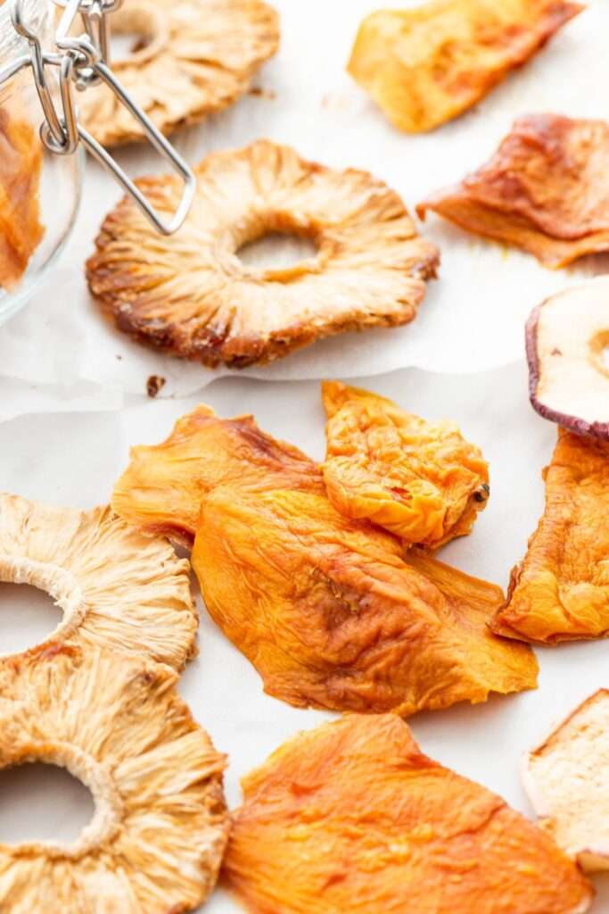 An assortment of dried fruit slices, including pineapple, mango, and apple, displayed on a white surface—perfect examples for your comprehensive guide to dehydrating with an air fryer.