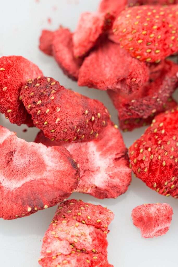 A close-up image showcases several pieces of freeze-dried strawberries, highlighting their bright red and lighter pink hues along with visible seeds—a perfect snapshot for a comprehensive guide on dehydrating fruits.