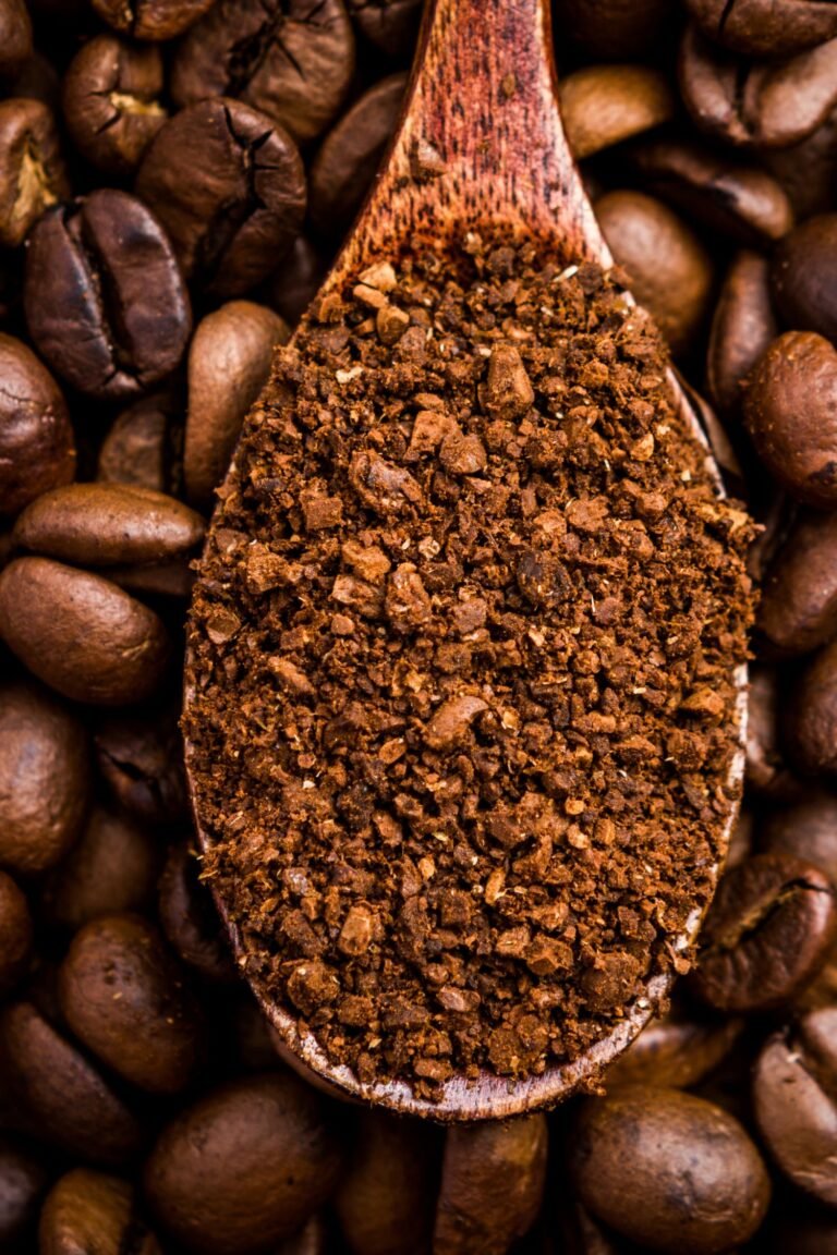 A wooden spoon filled with ground coffee rests on a bed of whole coffee beans.