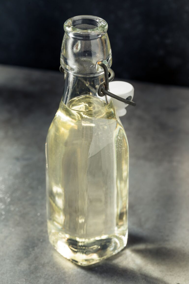 A clear glass bottle filled with the transparent liquid of simple syrup, sealed with a metal flip-top clasp on a gray surface.